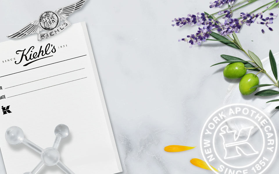Alt-tekst: Een collage met een zwart-wit foto van een apotheek, levendige bladeren en bloemen, en het logo van Kiehl's met de tekst "New York Apothecary Since 1851".