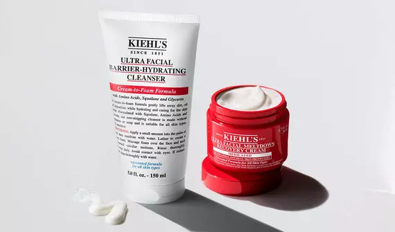 Twee Kiehl's Ultra Facial huidverzorgingsproducten: een witte tube Barrier-Hydrating Cleanser en een open rode pot Meltdown Recovery Cream op een witte achtergrond.