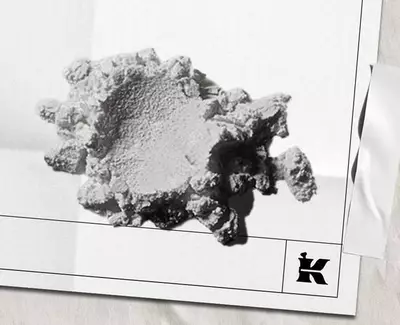 Een gestructureerd, onregelmatig gevormd wit fragment van een mineraal of materiaal, rustend op een lichte achtergrond, met een klein logo rechtsonder.
