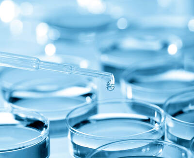 A close-up of a pipette dripping a drop of liquid into a series of blue petri dishes.