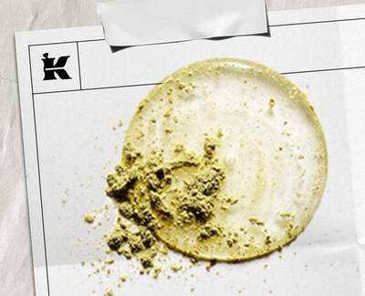 Une tache circulaire de creme claire avec un amas texture de poudre verte, presentee sur une feuille blanche marquee d'un logo.