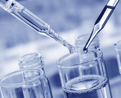 Close-up of two droppers, one releasing a drop, above a glass container with liquid, all in shades of blue.
