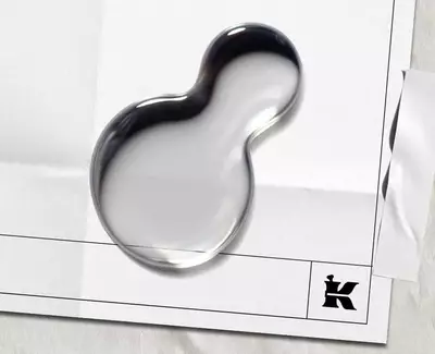 Twee druppels water op een leeg vel papier met een zwart "K"-logo en een stuk tape bovenaan.