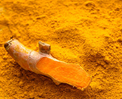 A piece of fresh turmeric root lies atop a mound of vibrant yellow turmeric powder.