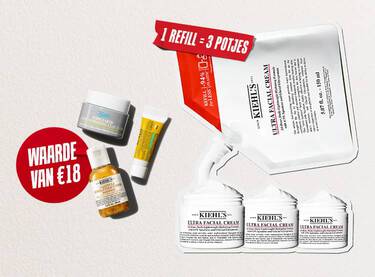 Drie reisformaat huidverzorgingsproducten van Kiehl's (de Ultra Facial Cream, de Calendula Herbal-Extract Toner en de Avocado Eye Cream) liggen verspreid op een witte, gestructureerde achtergrond. In het midden staat een rode, geverfde cirkel met de witte tekst "WAARDE VAN €18".