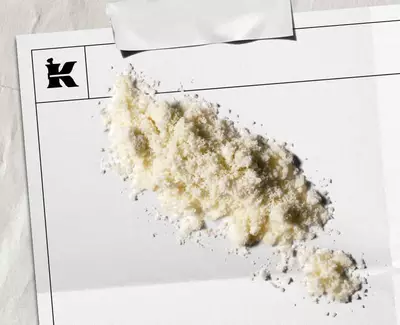 Een hoop wit poeder op een blanco vel papier met een logo in de hoek, wat een artistieke of stilistische presentatie suggereert.