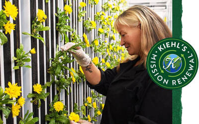 A woman in a black jacket gently tends to yellow flowers growing on vertical panels, with a logo for Kiehl's Renewal in the corner.