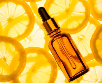 A brown glass dropper bottle placed on a bright background of lemon slices.