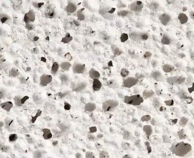 Close-up of a textured, porous white surface with numerous small holes and irregularities.