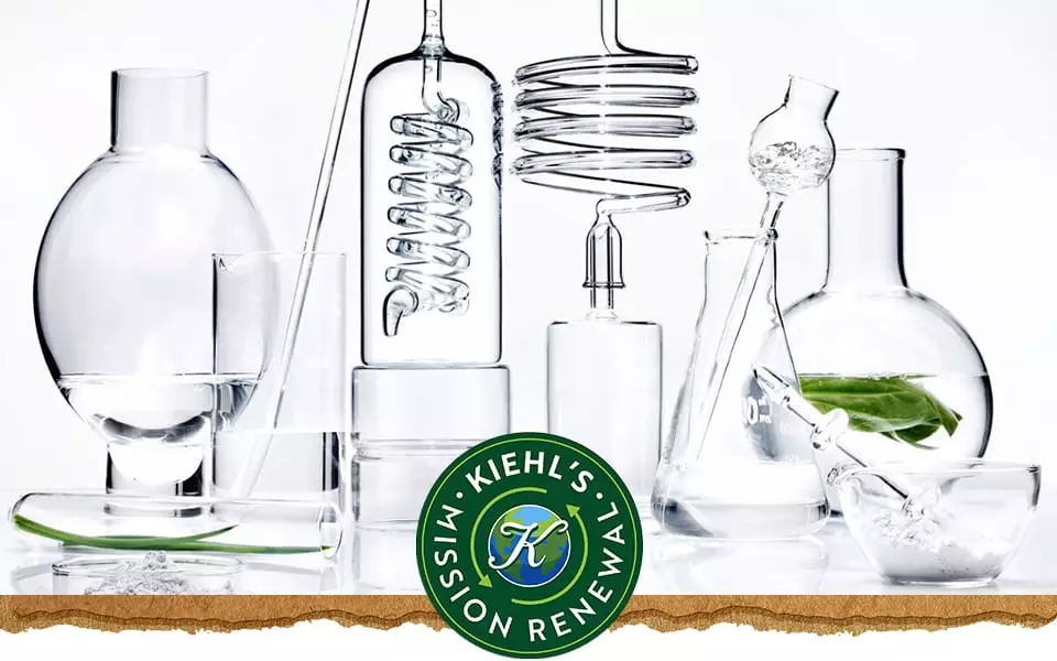 Une collection de recipients de laboratoire en verre transparent remplis d’eau et d’une feuille verte, avec le logo de Kiehl’s a droite.