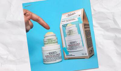 A hand points at a jar of Kiehl's Ultra Facial Cream next to its packaging, displayed on a crumpled background.