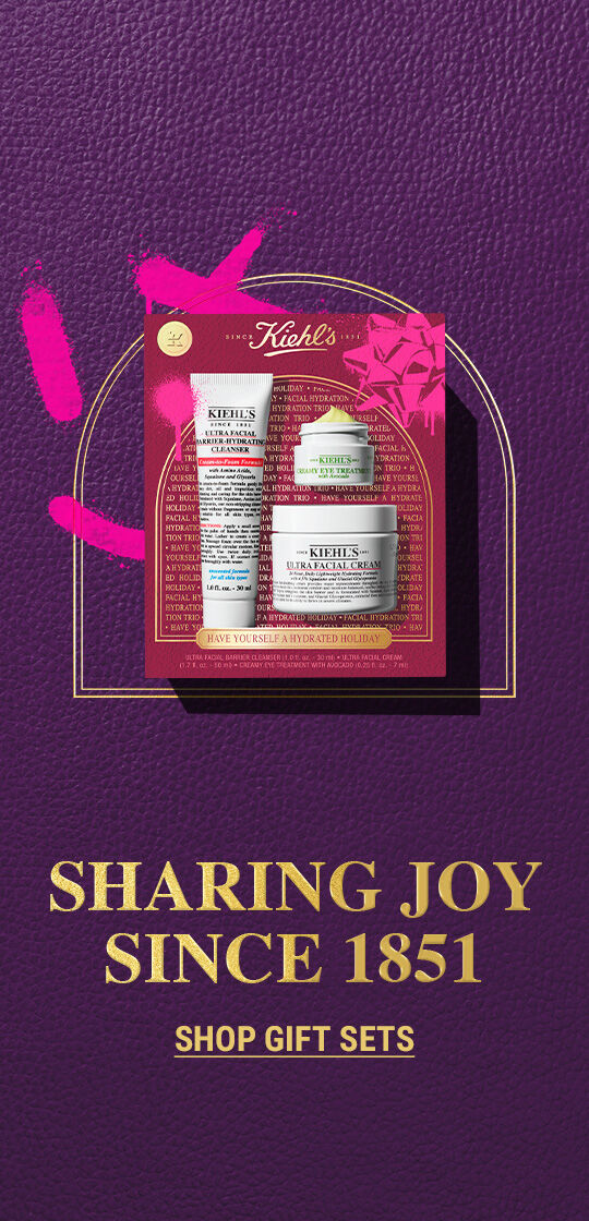 Kiehl's feestelijke geschenkset met een reiniger en gezichtscreme, tegen een rijke paarse achtergrond met gouden tekst. De slogan luidt: "Sharing Joy since 1951" (Vreugde delen sinds 1951)