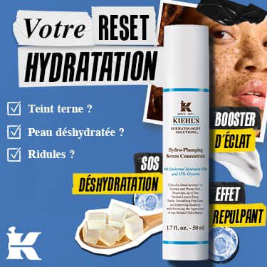 Une publicite promotionnelle sous forme de collage sur un fond bleu texture pour le soin Kiehl's Hydro-Plumping Serum Concentrate. En haut, une bande de papier dechire affiche le titre "Jouw HYDRATATIE-RESET", accompagnee d'une liste a cocher demandant "Doffe huid?" (Peau terne ?), "Gedehydrateerd?" (Deshydratee ?) et "Fijne lijntjes?" (Ridules ?). Au centre se dresse le flacon-pompe blanc du serum, entoure d'etiquettes colorees indiquant "DEHYDRATATIE SOS", "GLOW-BOOSTER" et "PLUMP EFFECT". En haut a droite, une photo d'une personne aux taches de rousseur est fixee avec du ruban adhesif noir, tandis qu'en bas, une cuillere en bois contenant des cubes de gel transparents cotoie des textures de gel liquide et le logo blanc "K" de Kiehl's dans le coin inferieur gauche.