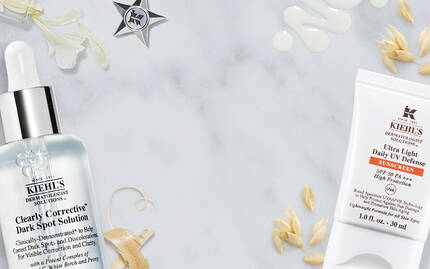 Produits de soin pour la peau de Kiehl's, dont un serum et une creme, presentes sur une surface en marbre avec des elements naturels.