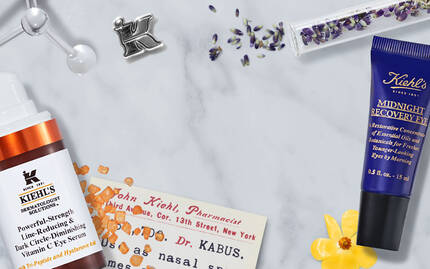 Produits de soin de la peau sur un fond en marbre, comprenant des flacons et des parfums, accompagnes de fleurs et de cristaux.