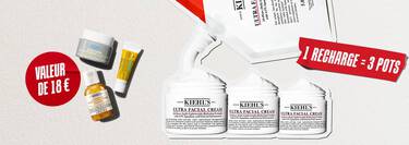 Trois produits de soin pour la peau Kiehl's en format voyage (la creme Ultra Facial Cream, la lotion Calendula Herbal-Extract Toner et le soin contour des yeux Avocado Eye Cream) sont disposes sur un fond blanc texture. Au centre, un cercle rouge peint a la brosse contient l'inscription en blanc "WAARDE VAN €18" (valeur de 18 €).