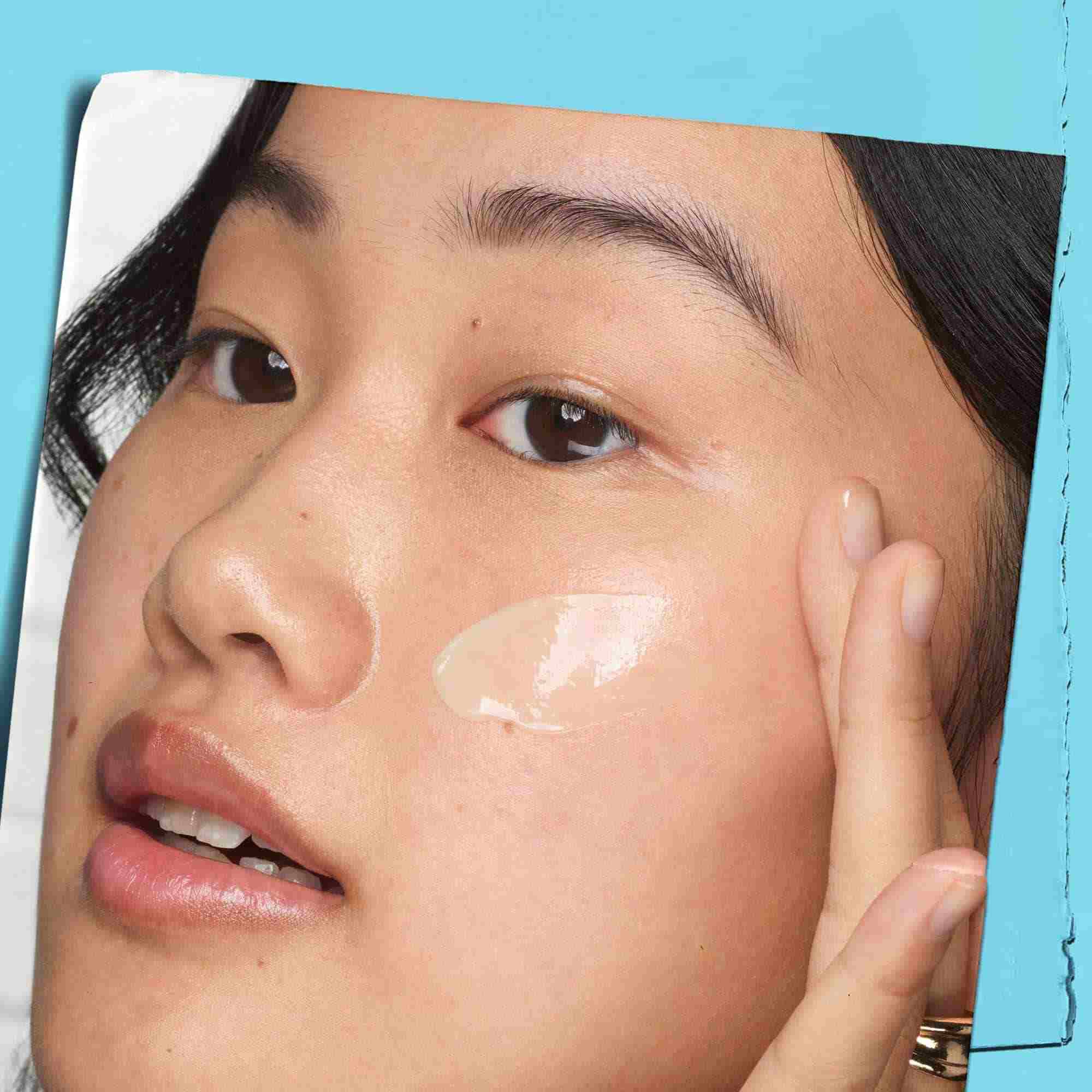 A graphic featuring a close-up of a person's face. A hand is gently touching the cheek, where a dab of light-colored product is visible. The image is set against a light blue background.