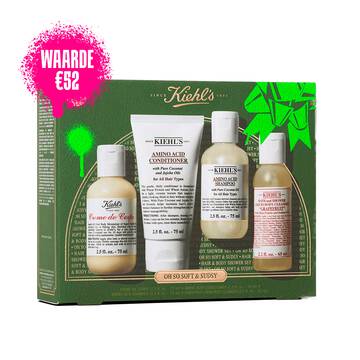 Een afbeelding met links een groene en gouden Kiehl's geschenkdoos met vier producten. Rechts van de doos staan dezelfde vier producten buiten de doos: een flesje "KIEHL'S CREME DE CORPS", een tube "KIEHL'S AMINO ACID CONDITIONER", een flesje "KIEHL'S AMINO ACID SHAMPOO" en een flesje "KIEHL'S GENTLY EXFOLIATING BODY SCRUB GRAPEFRUIT". De doos is versierd met felgroene grafische accenten en heeft onderaan de tekst "OH SOFT & SUDSY".